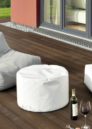 Dunkle Holzterrasse neben einem Gebäude mit Sitzkissen und dekorativen Elementen.