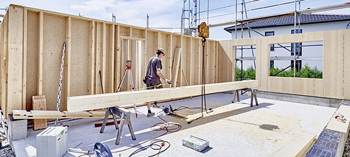 Holzrahmenbau eines Hauses, Arbeiter montiert Holzbalken auf der Baustelle.
