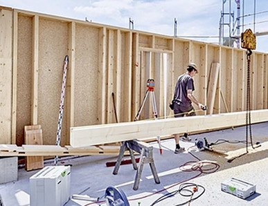 Holzrahmenbau eines Hauses, Arbeiter montiert Holzbalken auf der Baustelle.