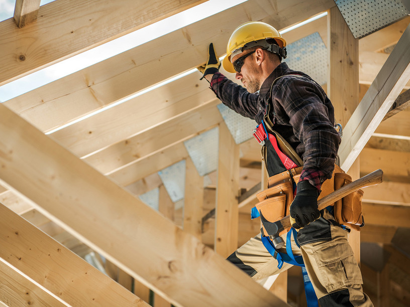 Zimmermann mit Schutzhelm und Werkzeug befestigt Konstruktionsvollholz (KVH) beim Bau eines Dachstuhls.