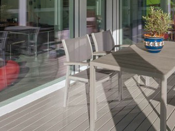 Überdachte Terrasse mit grauem Holzboden, modernem Esstisch-Set und Blick in den offenen Wohnbereich.