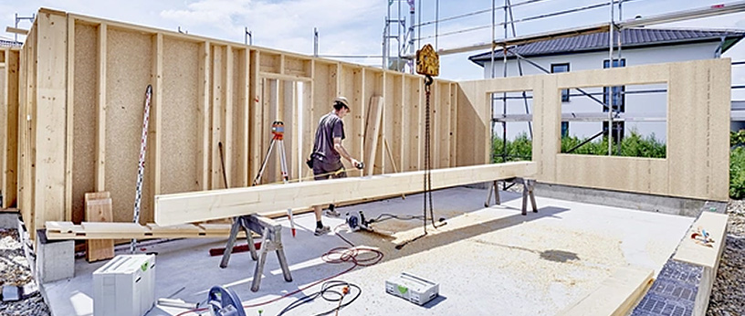Holzrahmenbau eines Hauses, Arbeiter montiert Holzbalken auf der Baustelle.